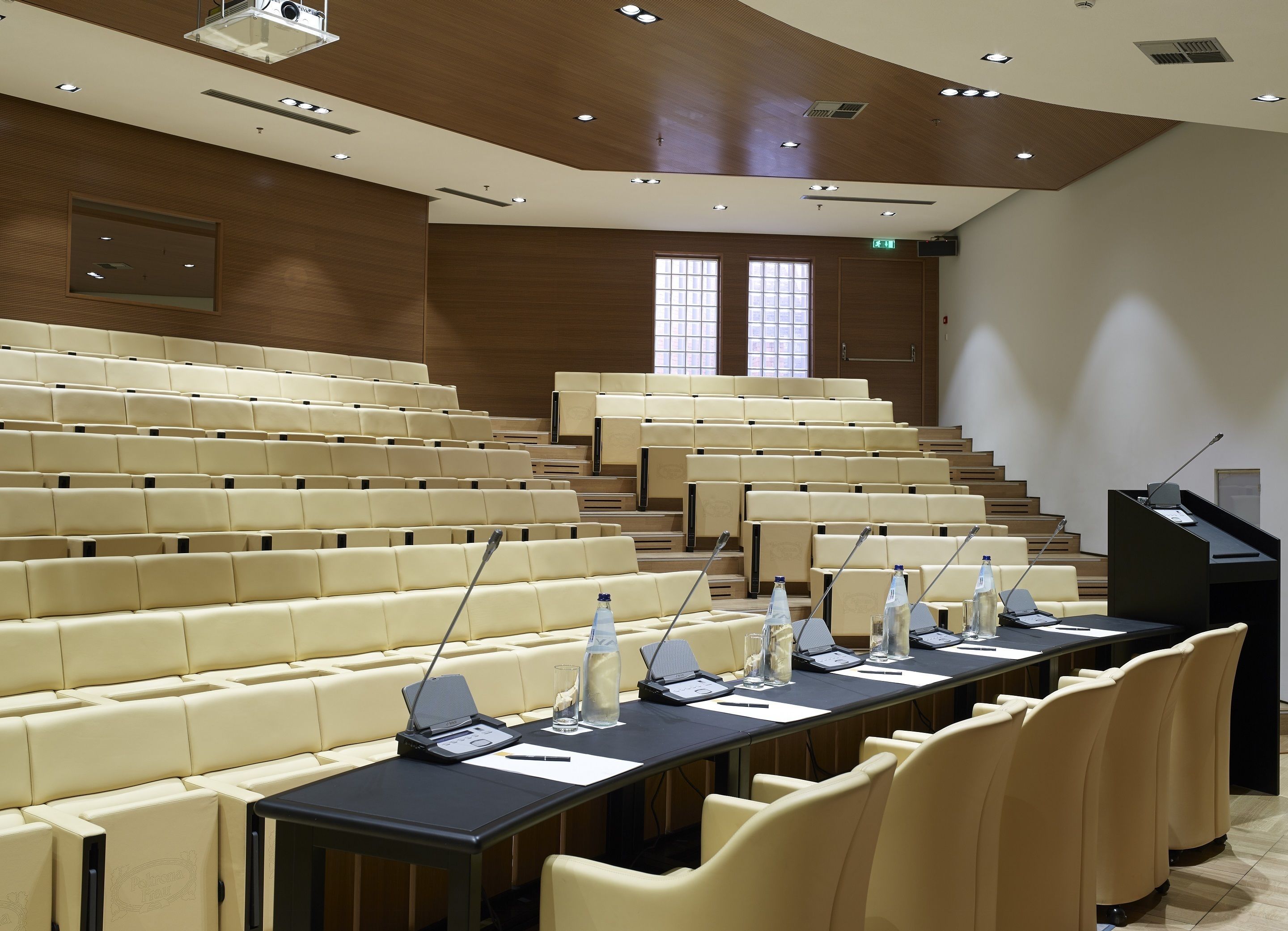Un salón de conferencias con asientos escalonados, un atril y una pantalla de proyector.