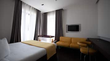 A hotel room with a bed, a sofa, a desk, and a TV.