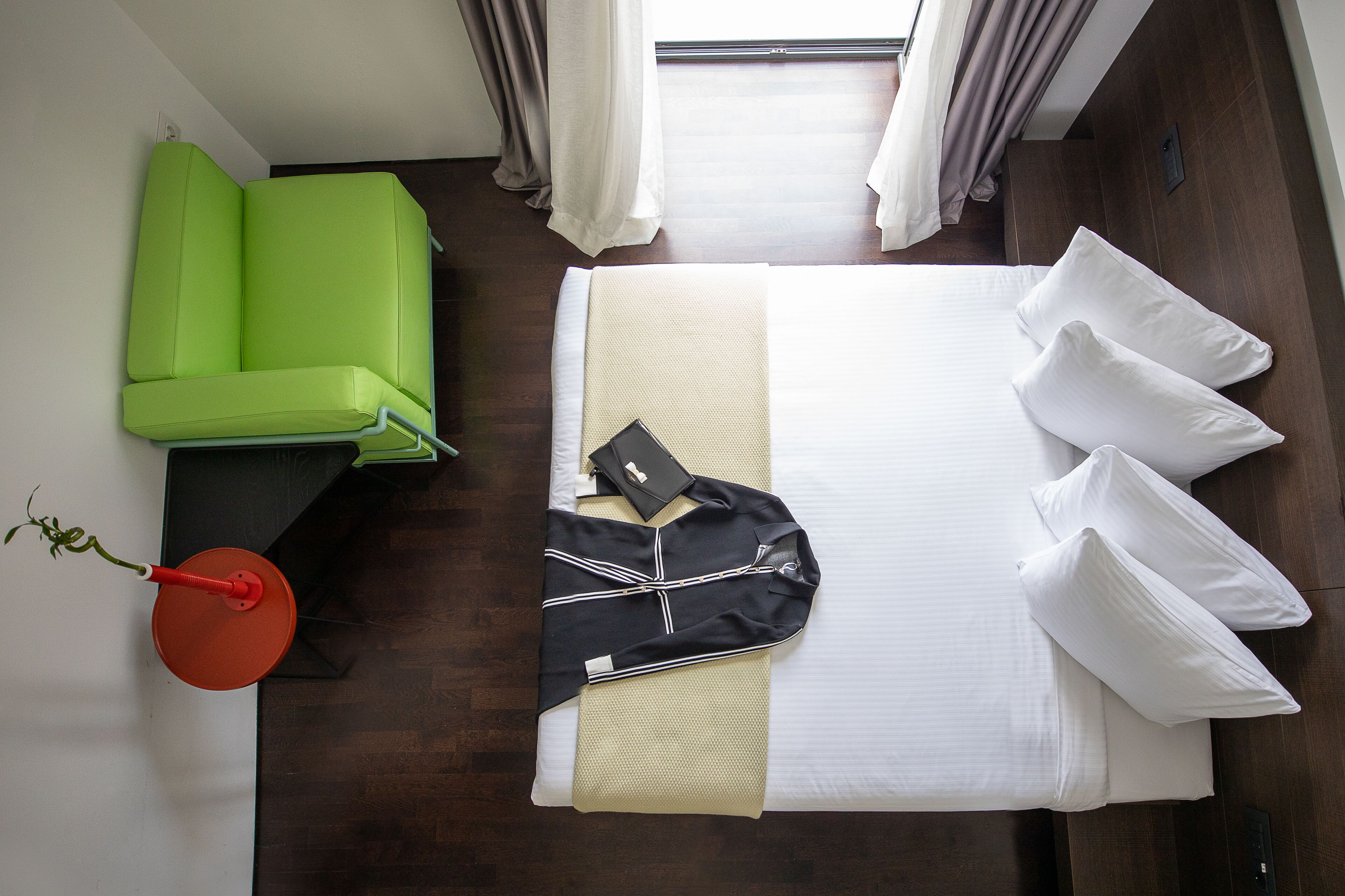 A hotel room with a bed, a green sofa, a small table with a red lamp, and a potted plant.