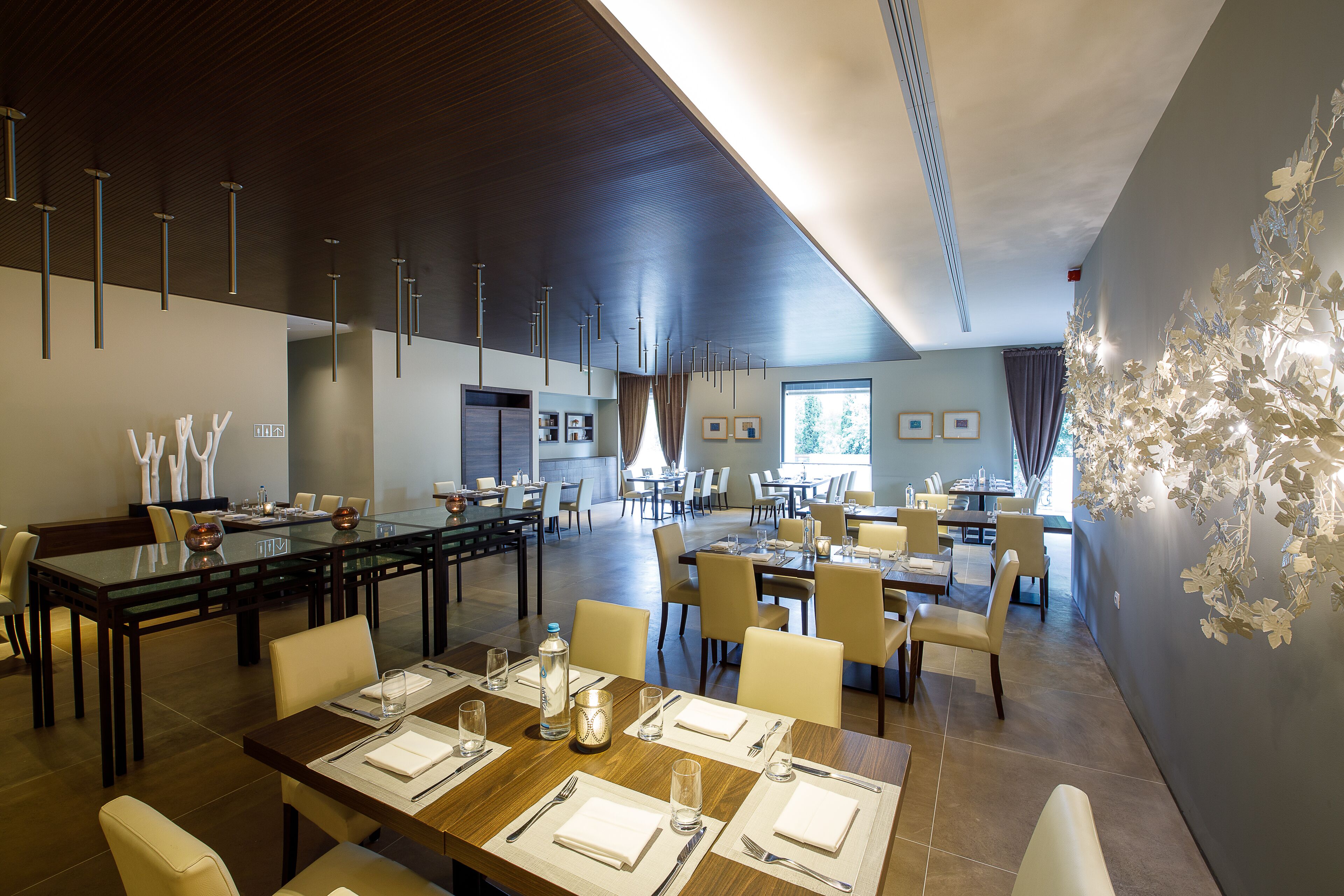 A spacious dining area with multiple tables and chairs, modern lighting fixtures, and a large window providing natural light.