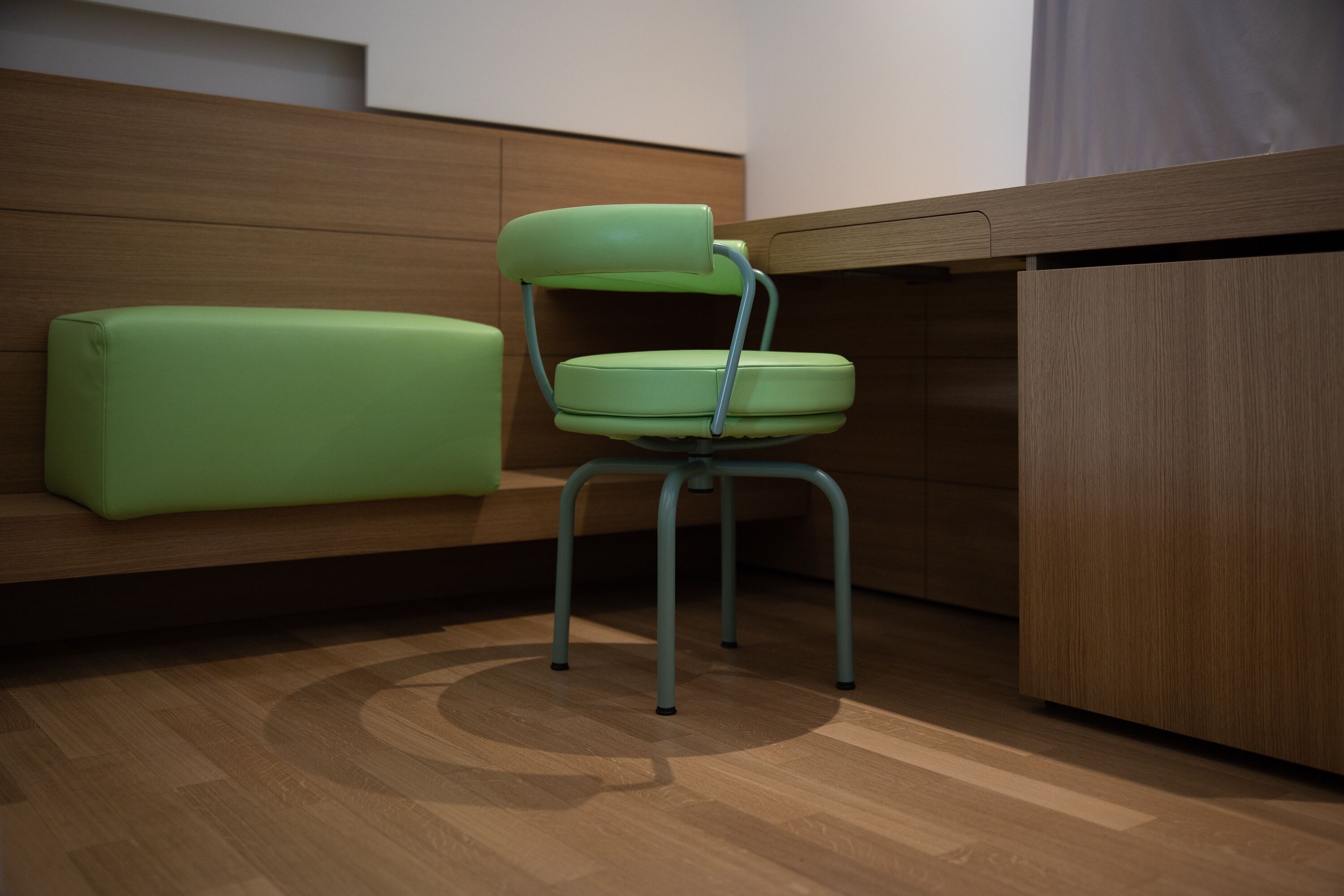 A modern room with a wooden floor, a green cushioned bench, and a metal-framed chair.
