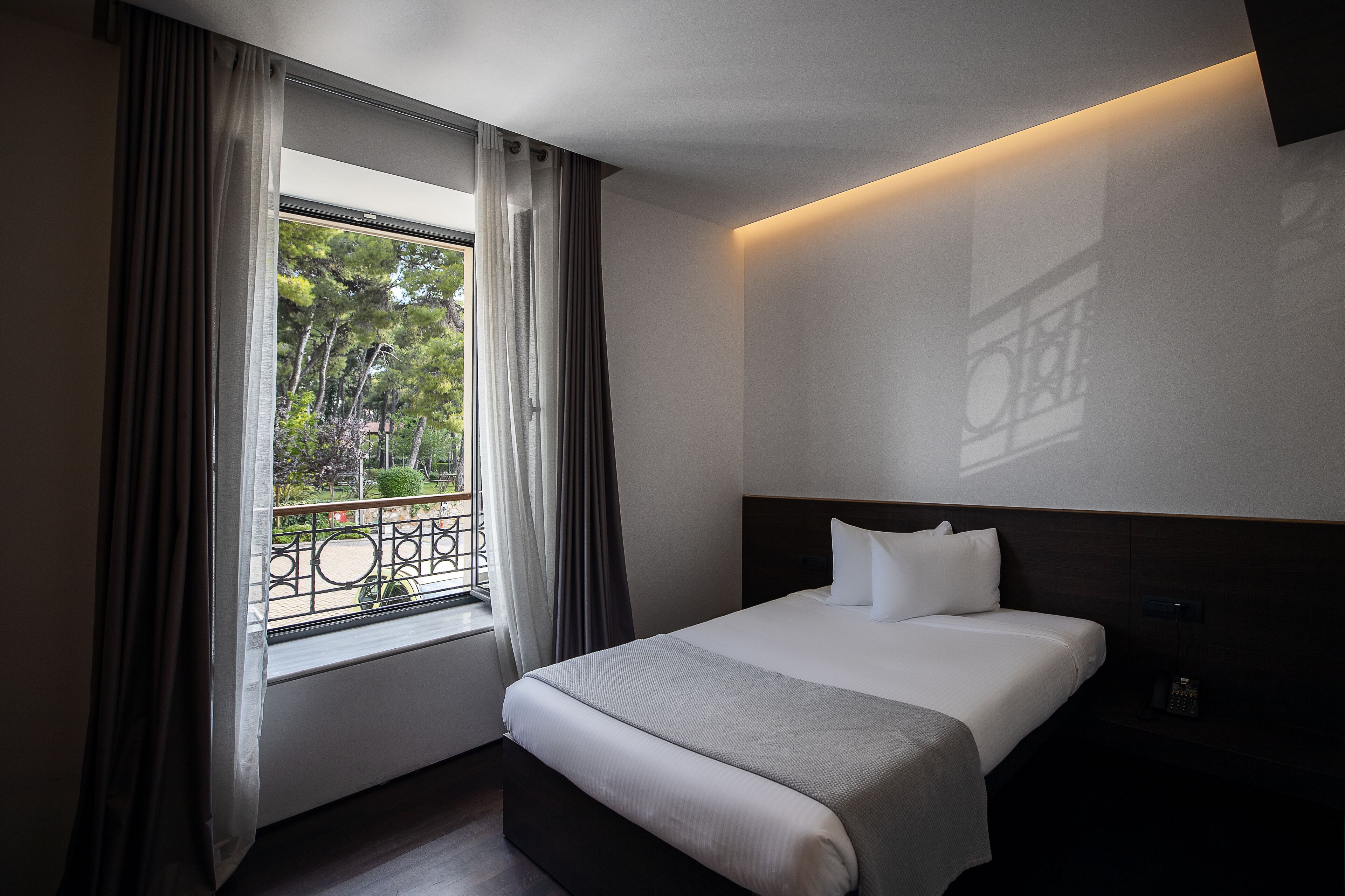 Een hotelkamer met een groot bed, een raam met gordijnen en uitzicht op bomen.
