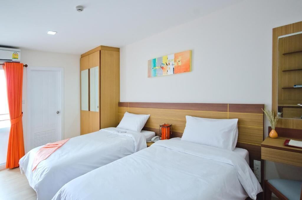 Una habitación de hotel con dos camas, cabecera de madera, mesita de noche con lámpara, un cuadro en la pared y un armario.