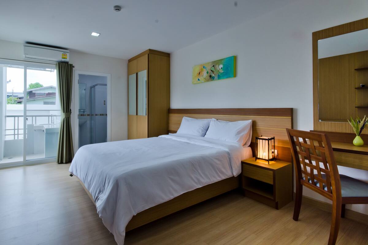 A hotel room with a bed, a desk, a chair, a TV, and a balcony.