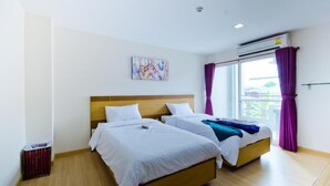 Habitación de hotel con dos camas, cabecero de madera, ventana con cortinas moradas y ventilador de techo.