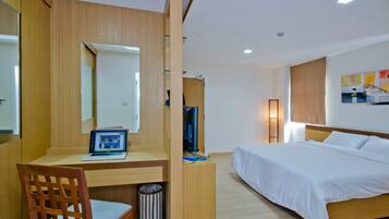 A modern hotel room with a wooden desk, a laptop, a bed with white linens, and a large mirror.