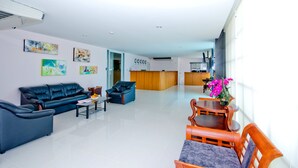 Un moderno vestíbulo de hotel con mostrador de recepción, zona de estar con sofás y una mesa de centro, y obras de arte en las paredes.