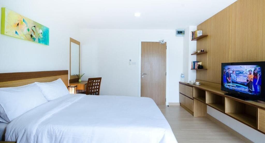 A hotel room with a large bed, a television, wooden furniture, and a painting on the wall.
