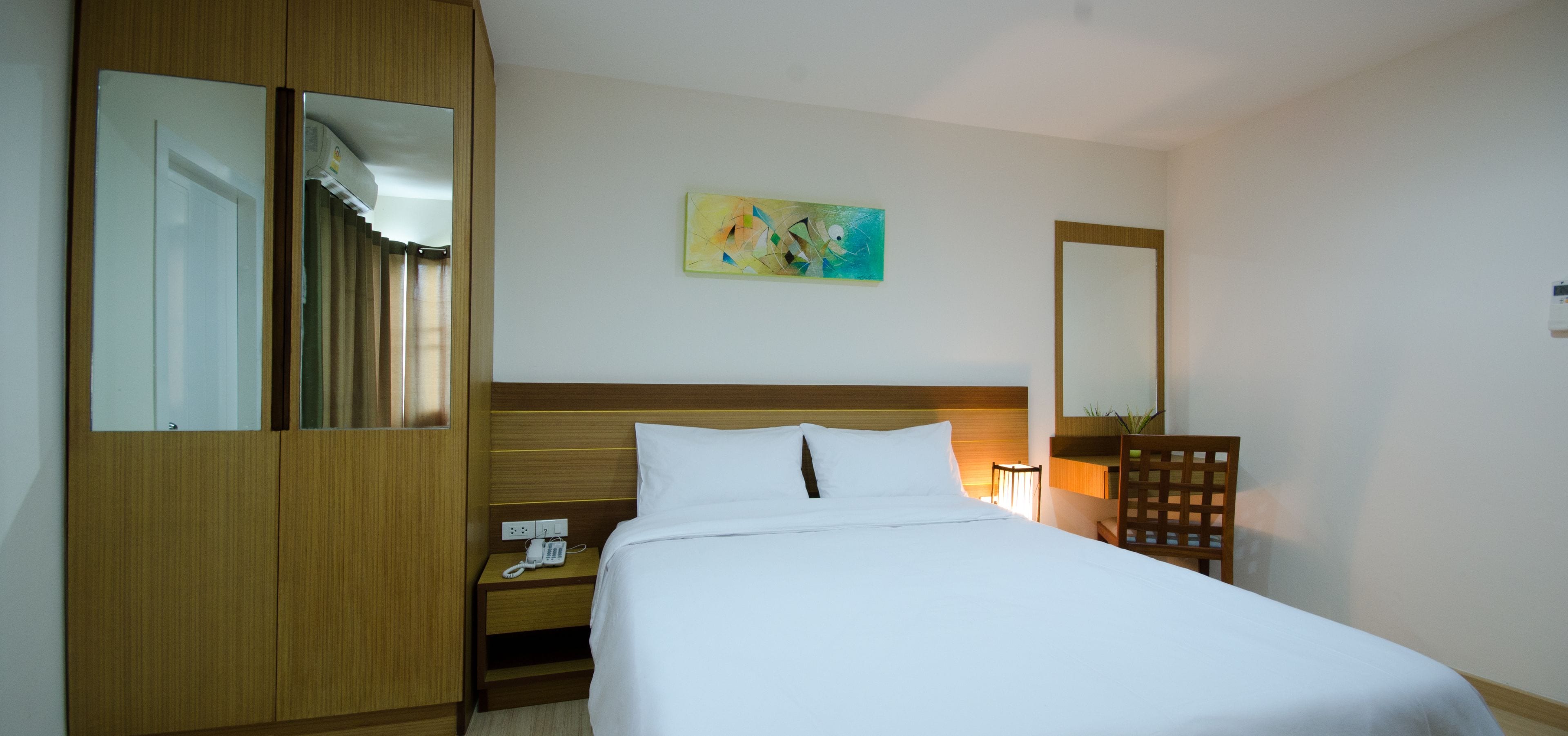 Une chambre d’hôtel avec un lit, une table de chevet avec un téléphone, un miroir et un tableau au mur.