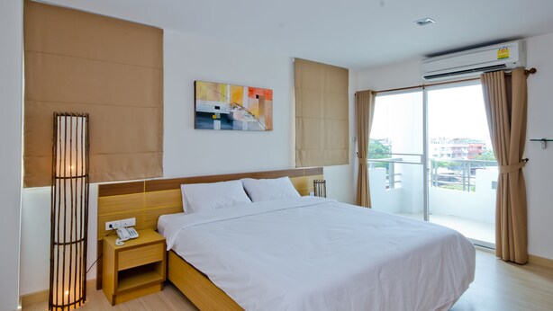 Una habitación de hotel con una cama grande, una mesita de noche con un teléfono, aire acondicionado instalado en la pared y vistas a la ciudad a través de la ventana.