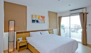 A hotel room with a large bed, a bedside table with a phone, a wall-mounted air conditioner, and a view of the city through the window.
