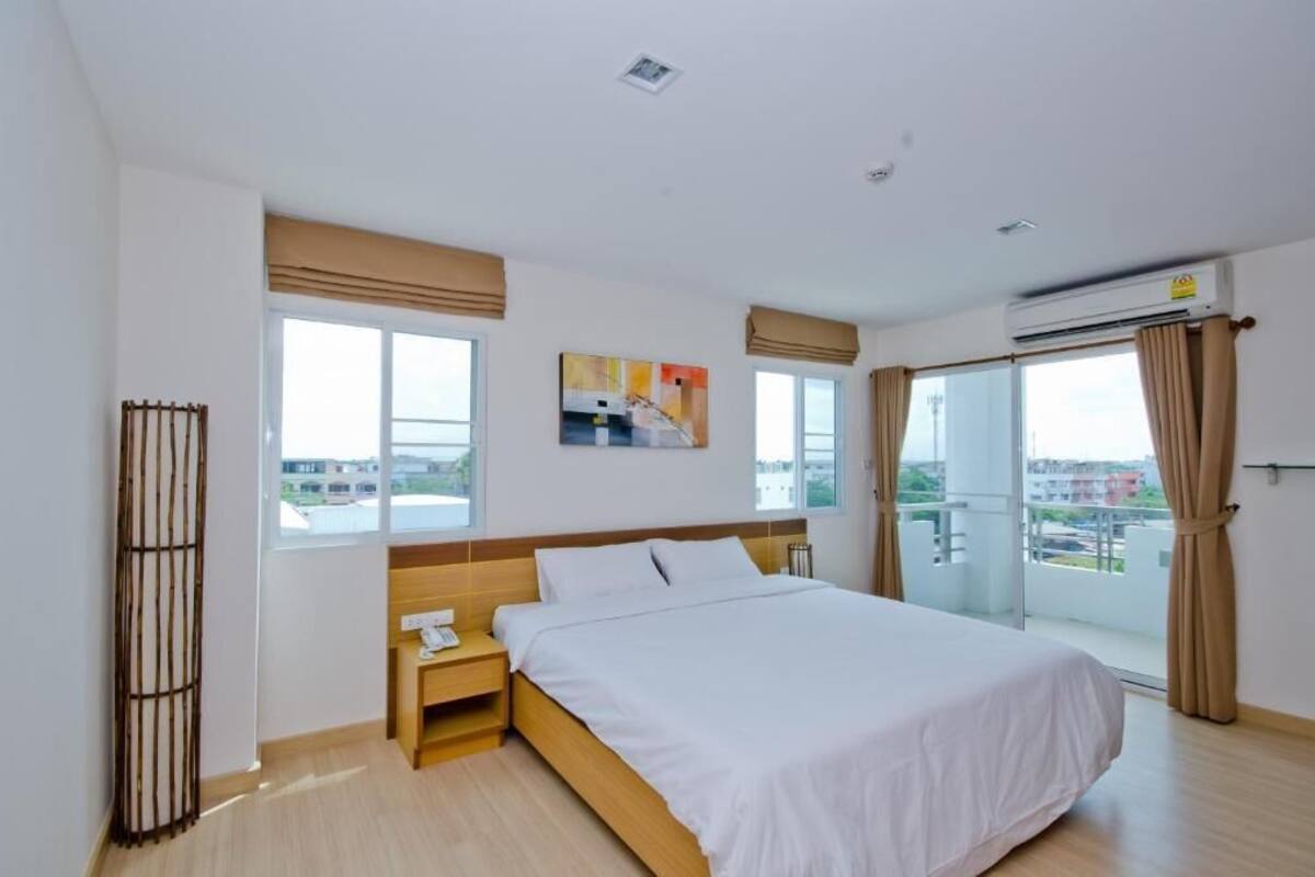 A modern hotel room with a large bed, a bedside table with a phone, a window with blinds, and a view of the city through the window.