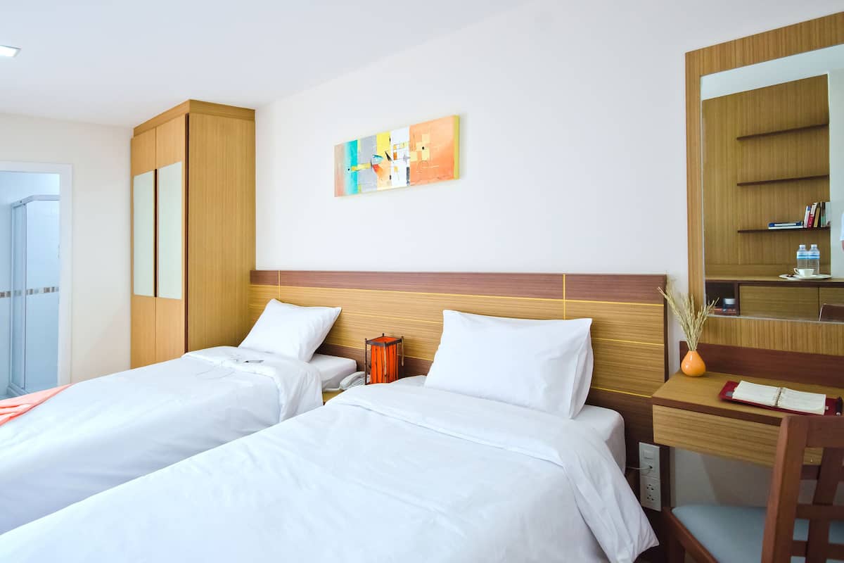 A hotel room with two beds, a wooden headboard, a small table with a vase, and a mirror.