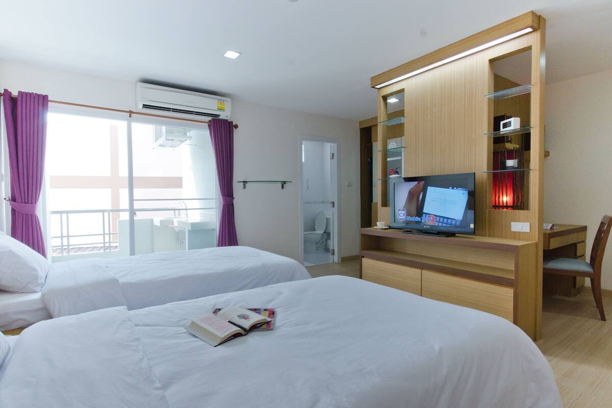 A hotel room with two beds, a TV, a desk, and a bathroom visible through an open door.