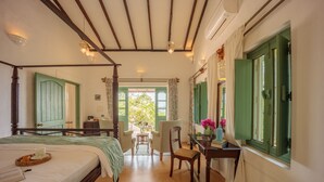 A four-poster bed with a green headboard, a wooden desk with a chair, and a view of the outdoors through a window with green shutters. - Wildflower Villas (Candolim)