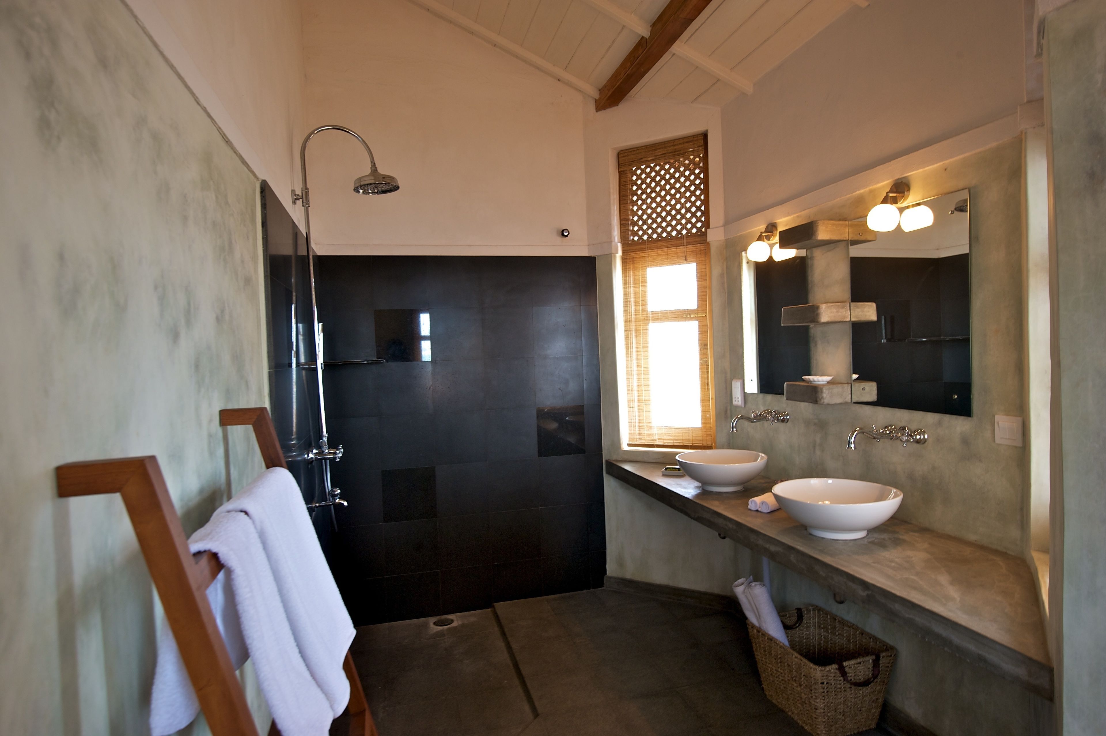 Une salle de bain moderne avec un espace douche aux couleurs sombres, un grand miroir et deux lavabos.