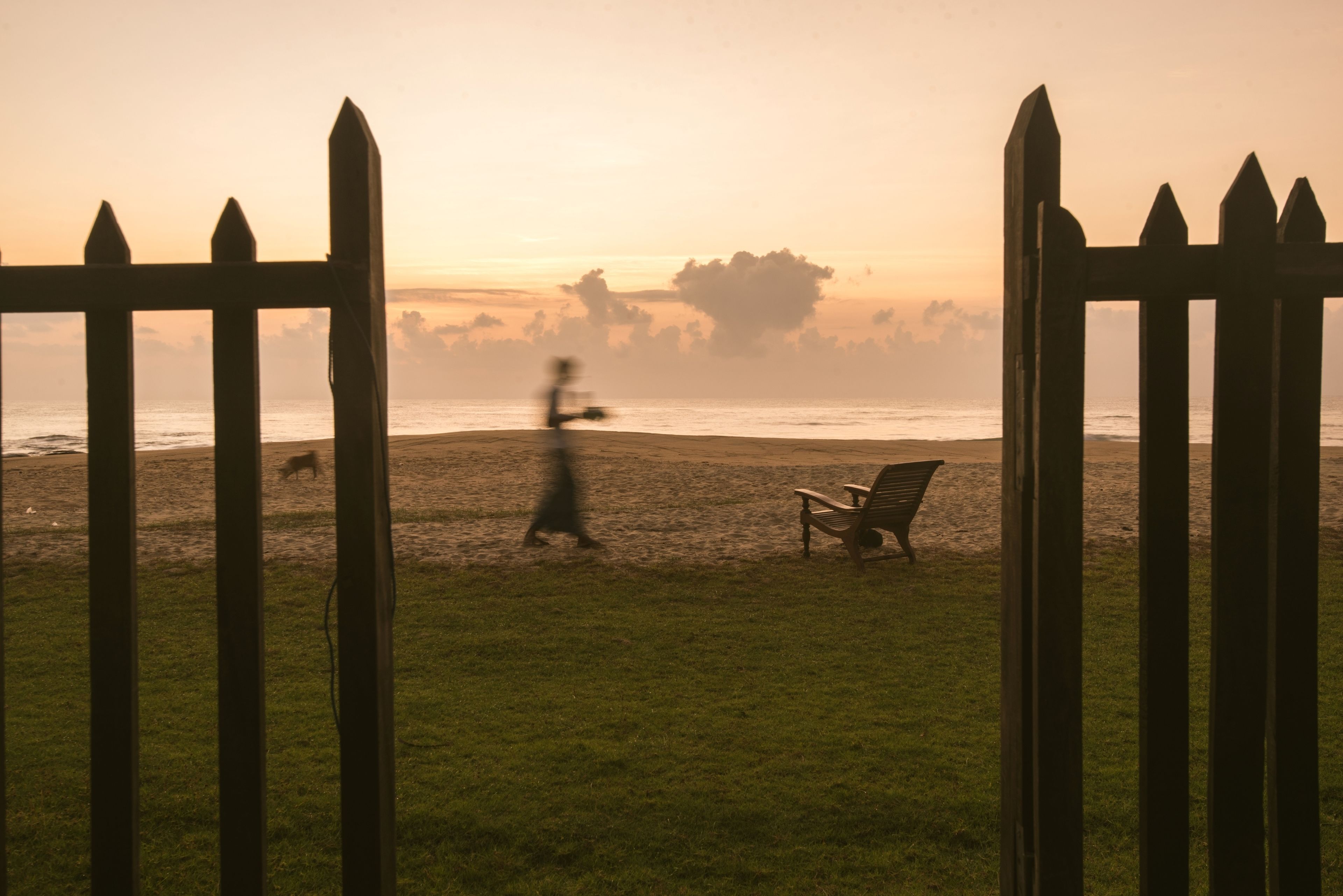 A beach view with a wooden fence, a bench, and a grassy area.