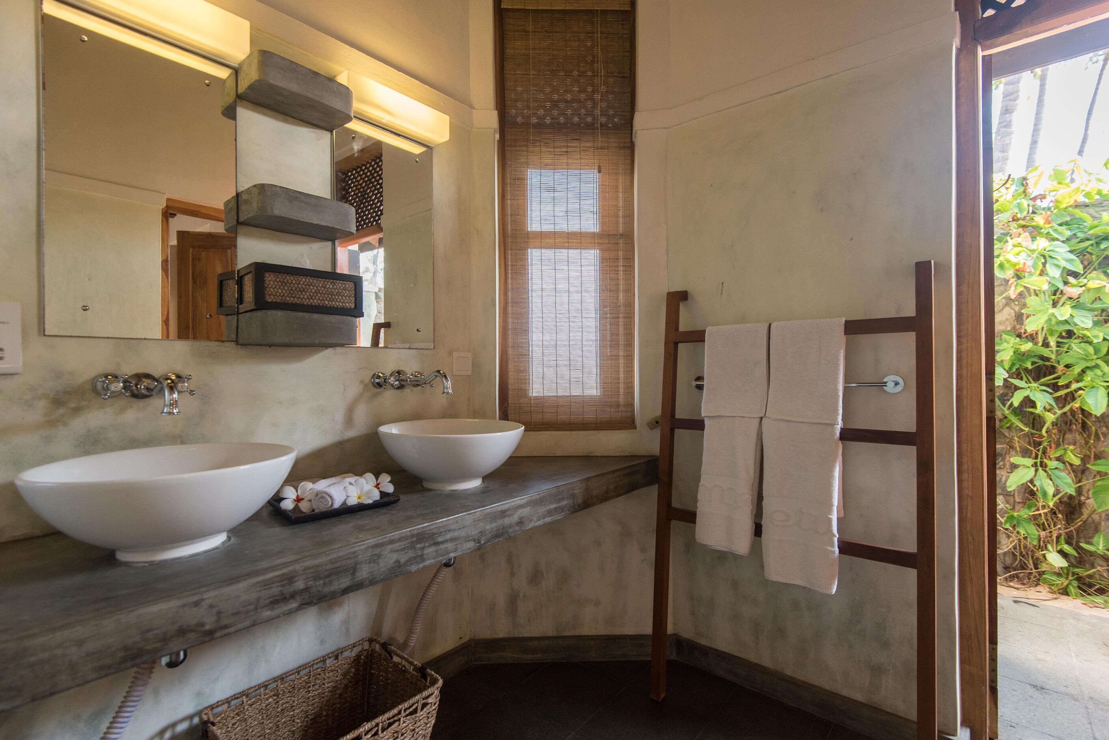 Un baño con dos lavamanos, un espejo, un perchero para toallas y una ventana con persianas.