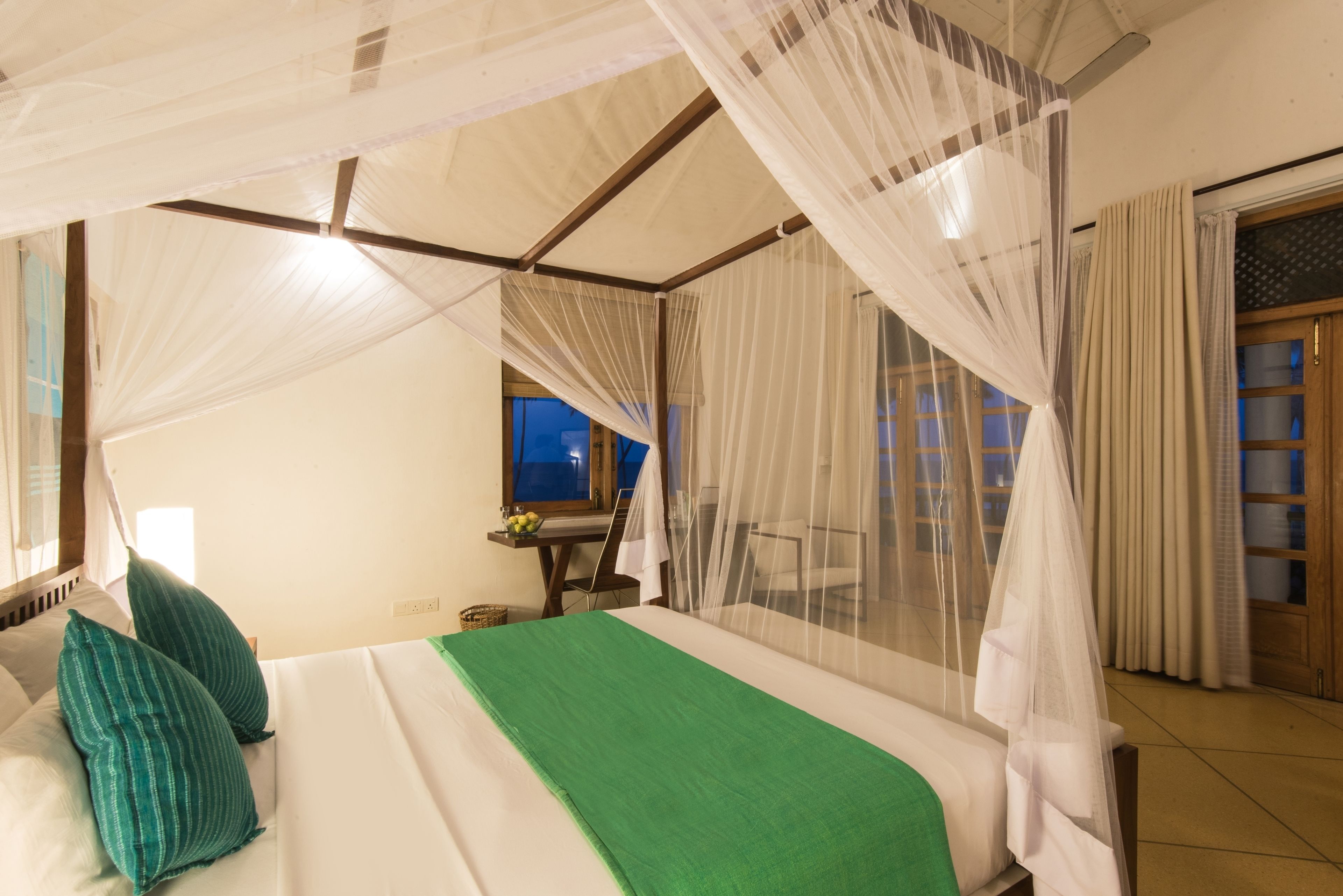 A bedroom with a canopy bed, a green bedspread, and a view of the outside through a window.