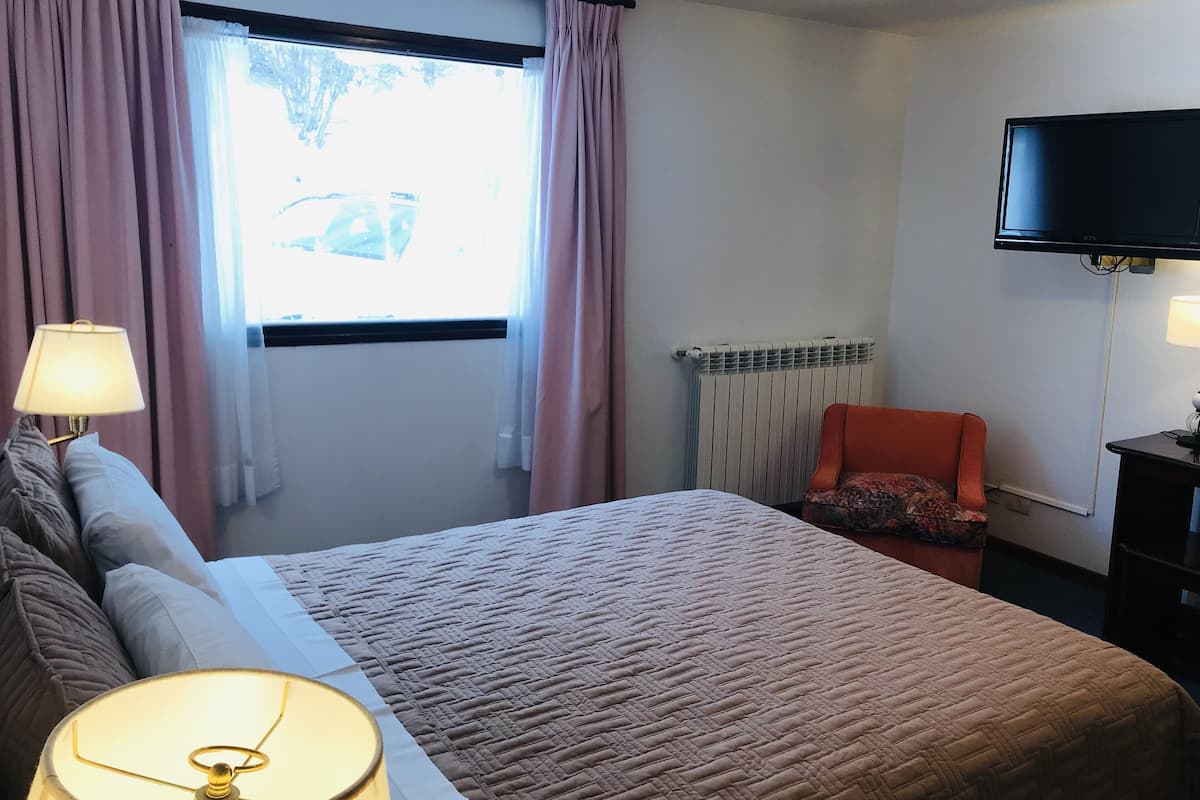 Habitación de hotel con cama, una silla, televisor y ventana con cortinas.
