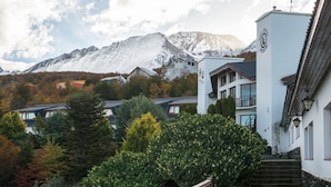 Un resort de montaña con picos nevados al fondo, un jardín cuidado y una escalera que conduce a un edificio con un letrero que indica que es un hotel.