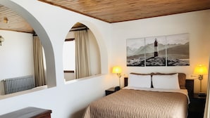 Habitación de hotel con una cama grande, dos lámparas de noche, un escritorio de madera, un radiador y un cuadro de un faro.