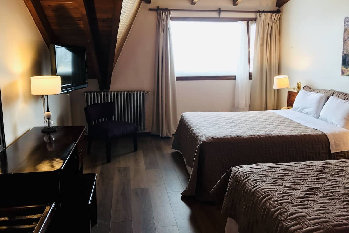 Habitación de hotel con cama, escritorio con lámpara, una silla, radiador y televisor en la pared.