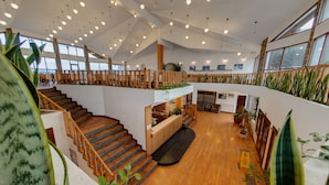 Un interior espacioso, distribuido en varios niveles, con suelo de madera, una escalera central y un entrepiso.