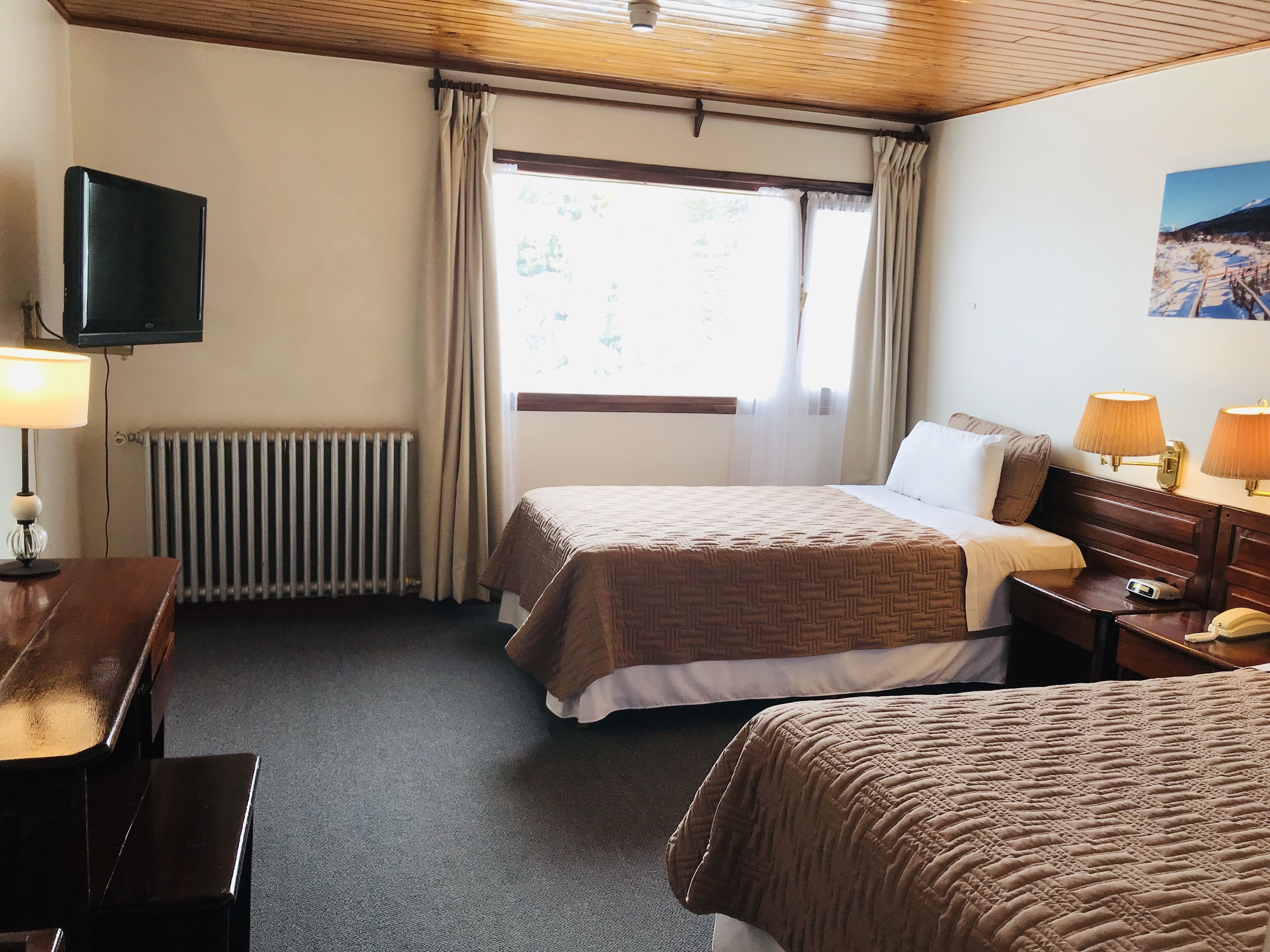 Habitación de hotel con dos camas, televisión, escritorio y ventana con cortinas.