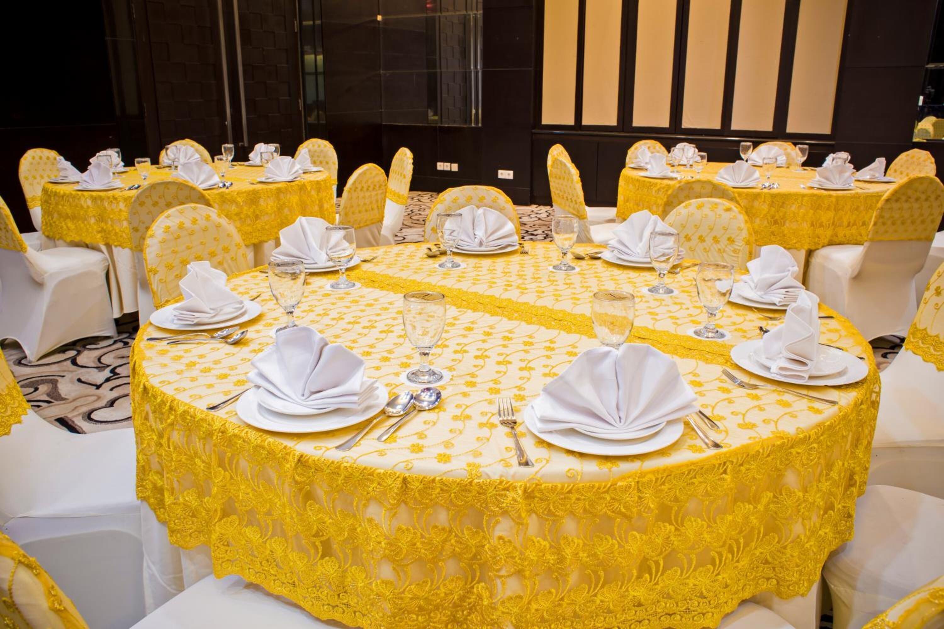 Une salle de banquet avec des tables rondes dressées pour le repas, chacune étant recouverte d’une nappe blanche et agrémentée de housses de chaise jaunes.