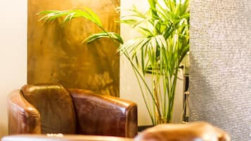 Un fauteuil en cuir, une grande plante verte et un mur à la texture intéressante.