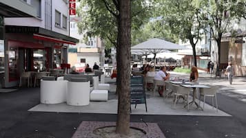 Un espacio al aire libre con mesas y sillas blancas, un árbol y un cartel para Hotel Elite.