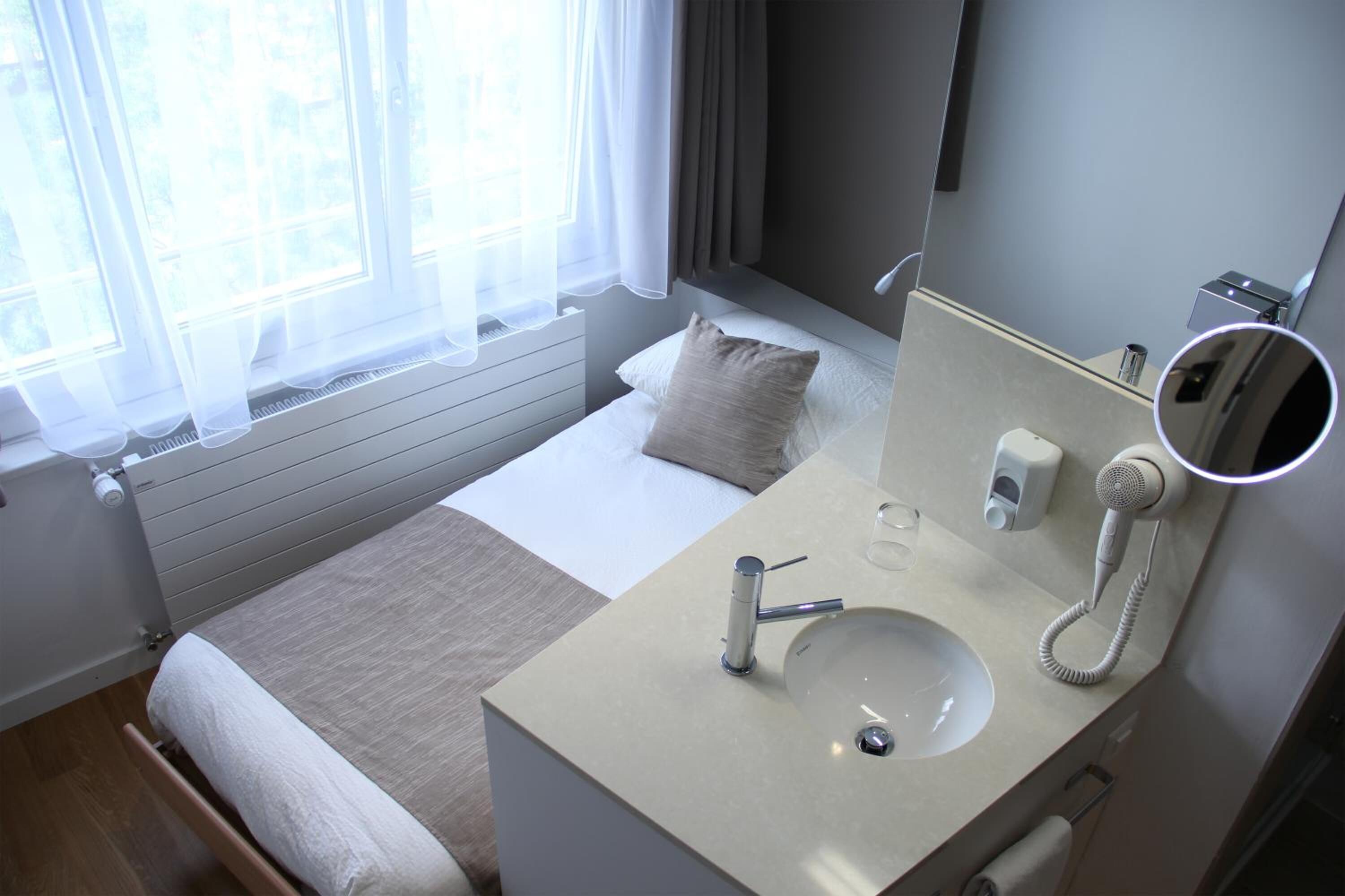 A modern hotel room with a bed, a bathroom with a sink, a mirror, and a hairdryer.
