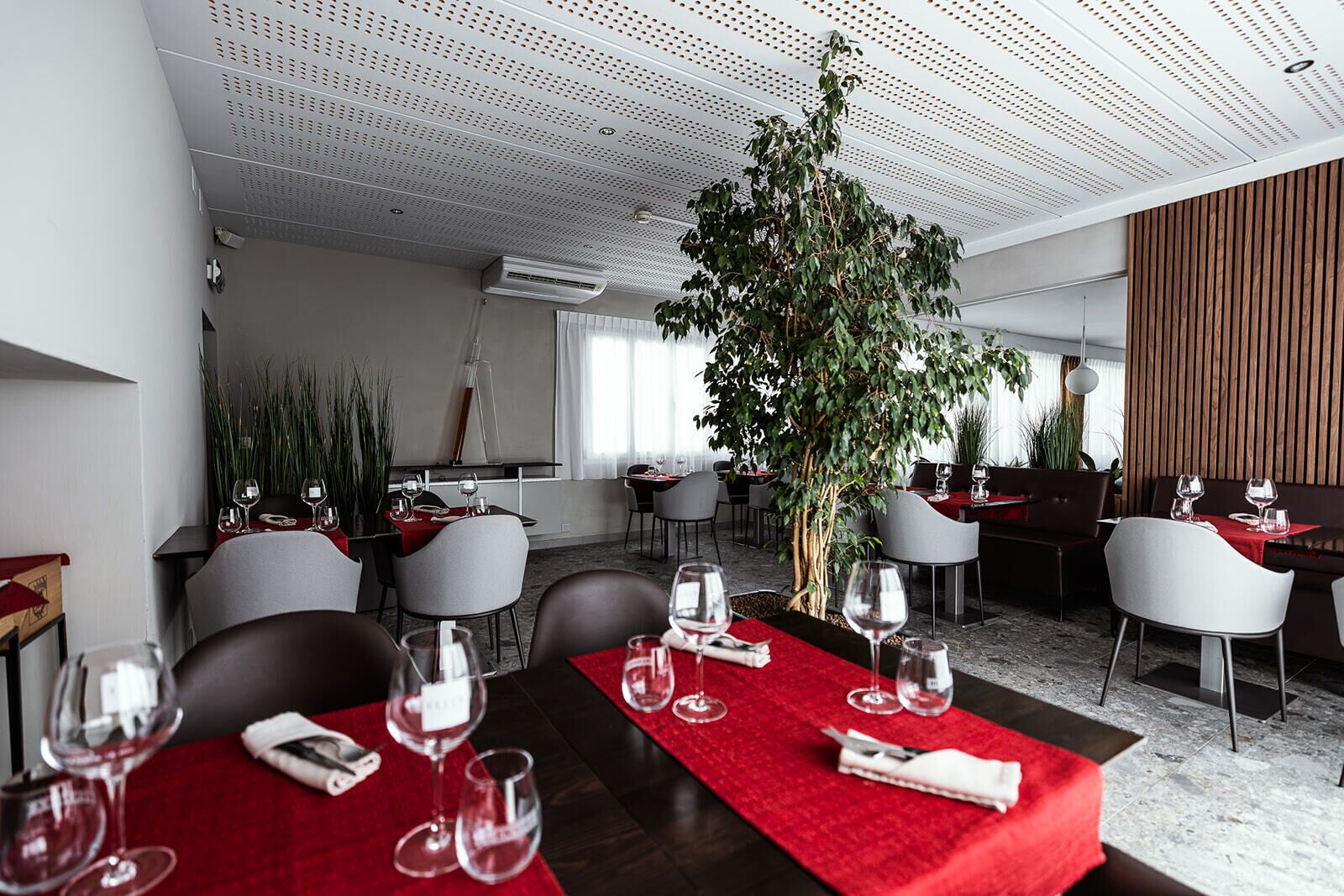 A modern dining area with tables set for two, featuring red tablecloths and wine glasses.