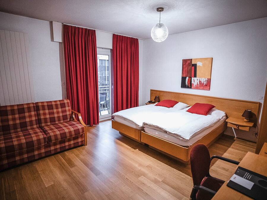 A hotel room with a bed, a sofa, a desk, and a red curtain.