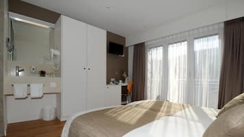 Een hotelkamer met een groot bed, een bureau met stoel, een badkamer met spiegel en een televisie.
