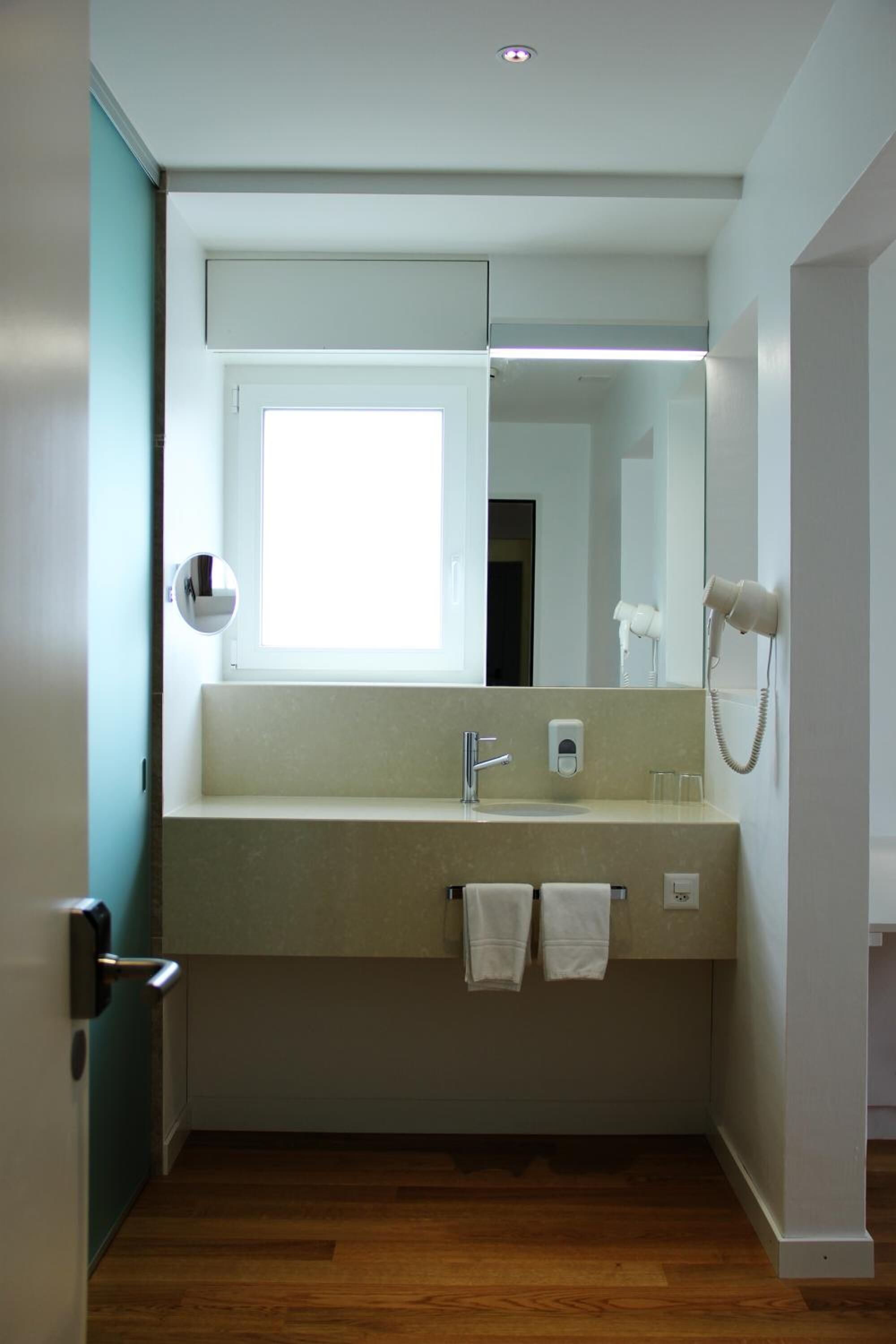 A modern bathroom with a large mirror, a sink, a hairdryer, and a towel rack.