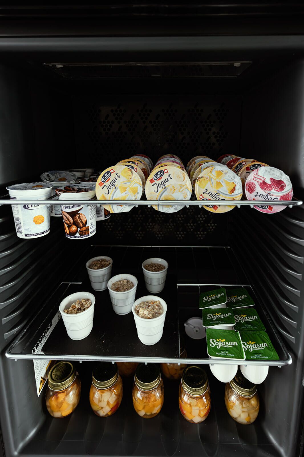 A refrigerator stocked with various food items including yogurt, granola, and jars of preserved fruit.