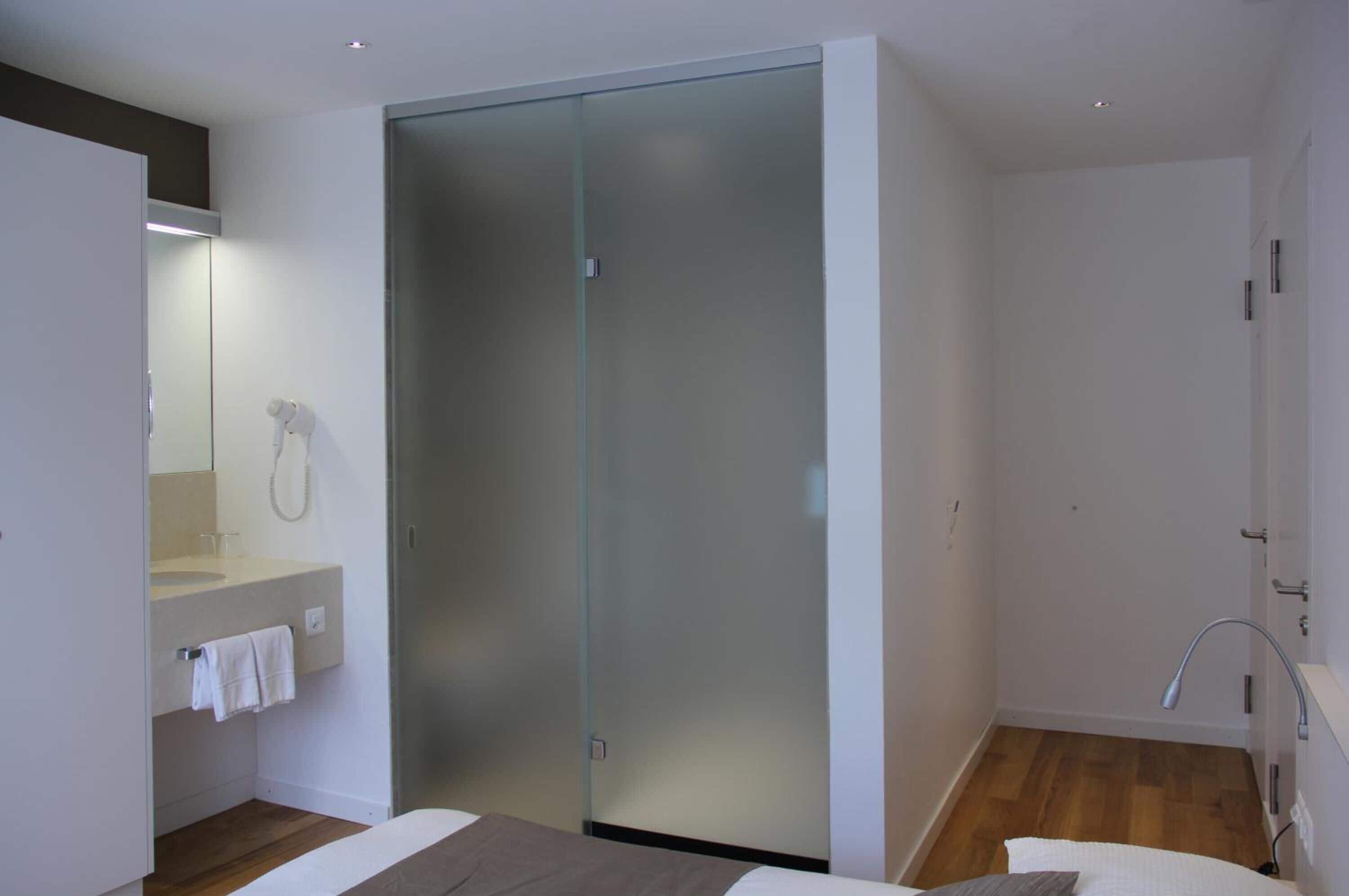 A modern bathroom with a glass shower enclosure, a sink with a towel rack, and a wooden floor.