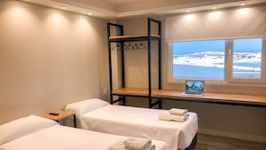A hotel room with two beds, a wooden desk, a laptop, and a window with a snowy view.
