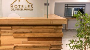A reception desk with a wooden design, a glass partition, and a sign reading "HOTELES DEL FIN DEL MUNDO" with a mountain graphic.