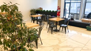 A modern indoor seating area with tables and chairs, potted plants, and a fire extinguisher.