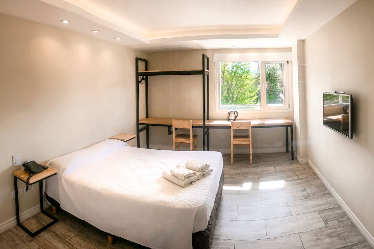 Un dormitorio con cama, escritorio, silla, televisor y ventana con vistas a zonas verdes.