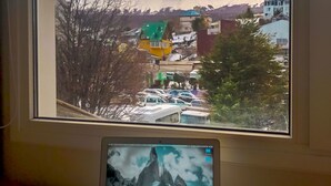 A laptop on a desk with a view of a snowy mountain and buildings through a window.