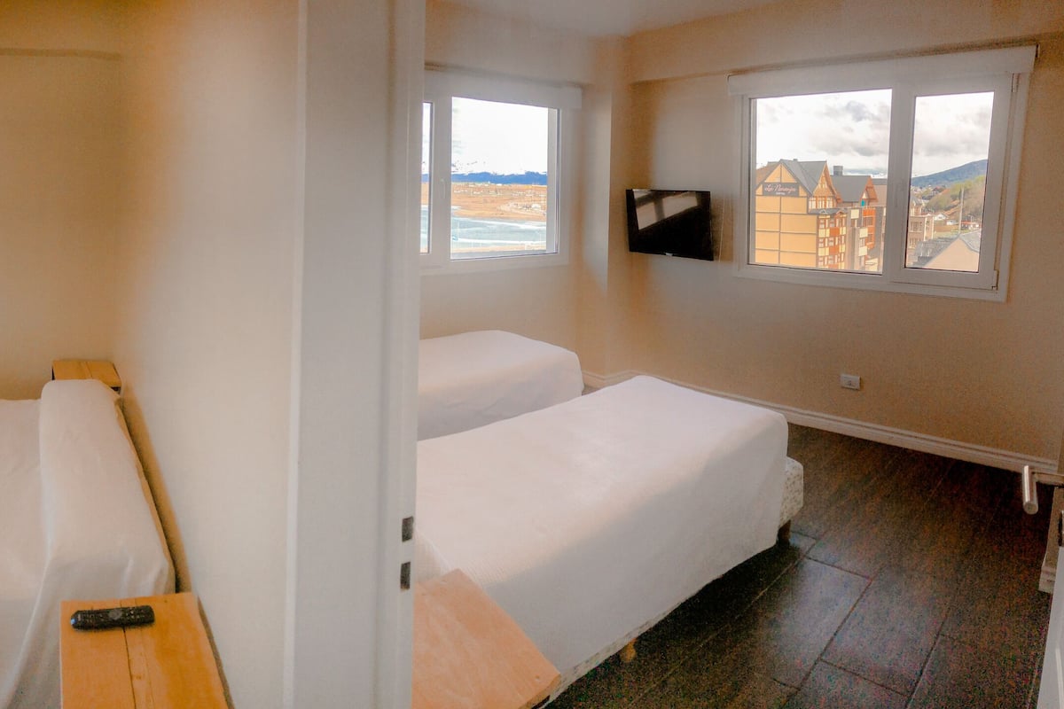 Una habitación con dos camas, una mesita y un televisor en la pared.
