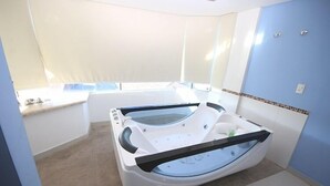 A modern bathroom with a large bathtub, a separate shower area, and a window providing natural light. - Emirates Hotel & Suítes (Santana do Livramento)