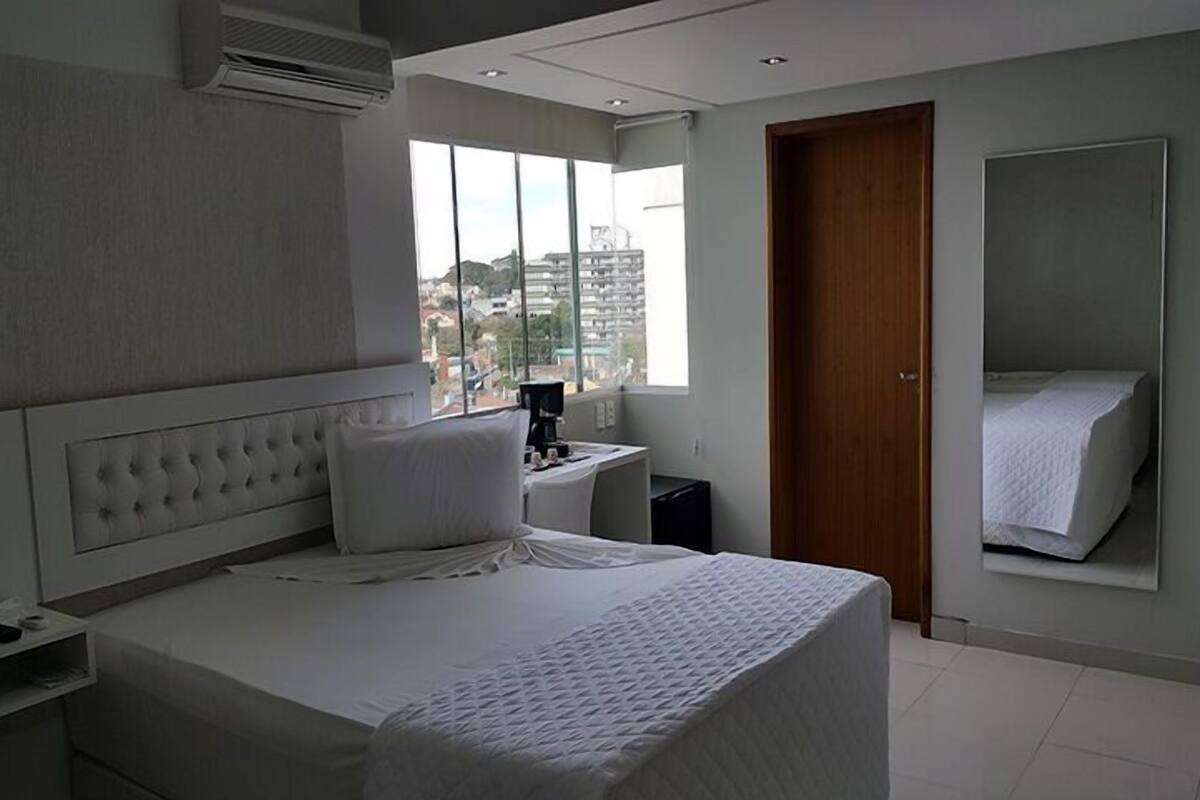 Een moderne hotelkamer met een groot bed, een nachtkastje, een spiegel en een raam met uitzicht op de stad.