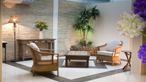 A lobby with wicker furniture, a stone wall, and a potted plant. - Emirates Hotel & Suítes (Santana do Livramento)