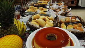 A buffet with various food items including bread, pastries, and a flan dessert. - Emirates Hotel & Suítes (Santana do Livramento)