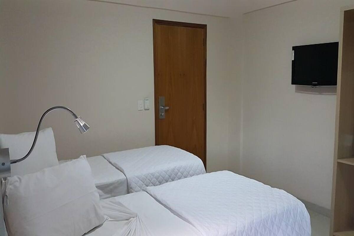 Een hotelkamer met twee bedden, een houten deur, een televisie aan de muur en een bedlampje.